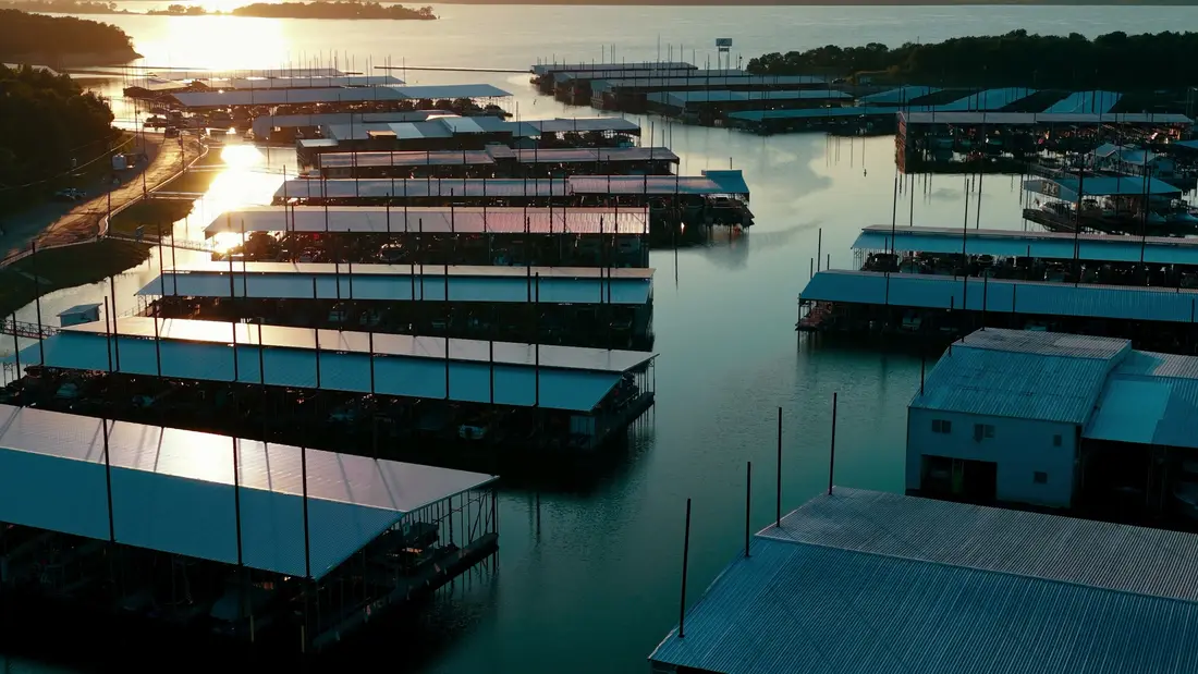 Aerial still over a lakeside marina at sunset, rows of covered boat slips on the water