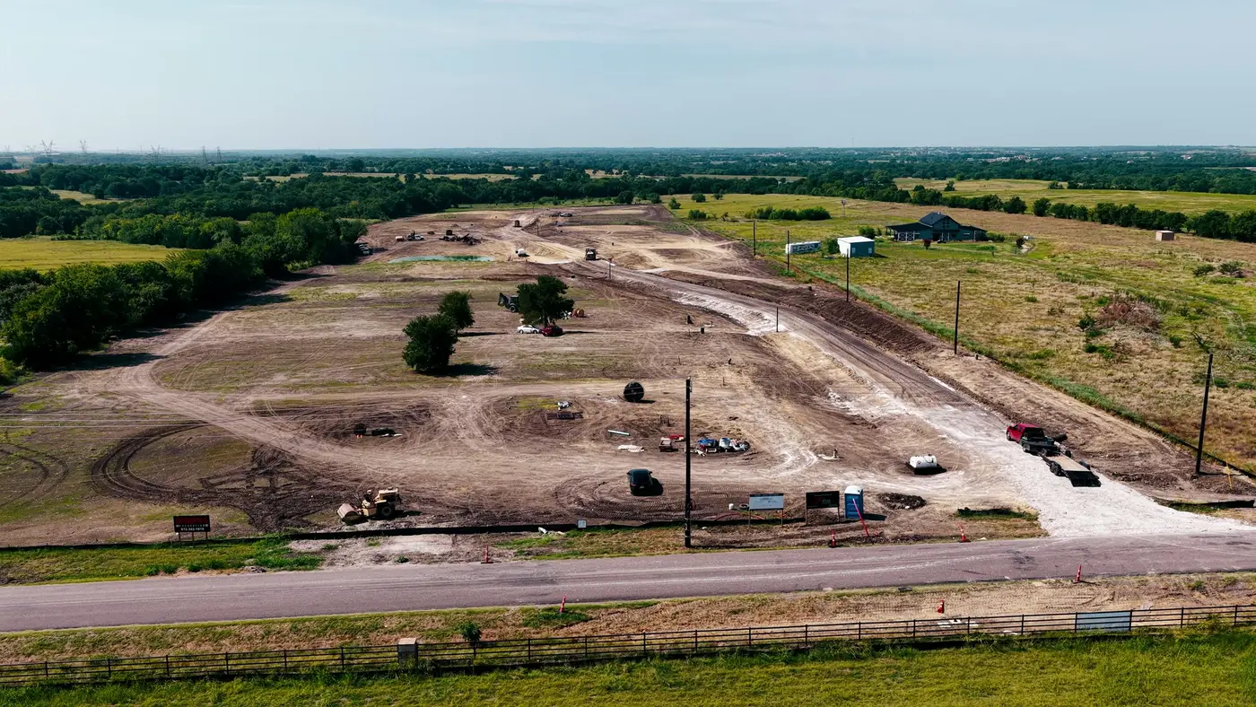 Aerial still over a land development in progress: graded lots, equipment on site and open fields beyond