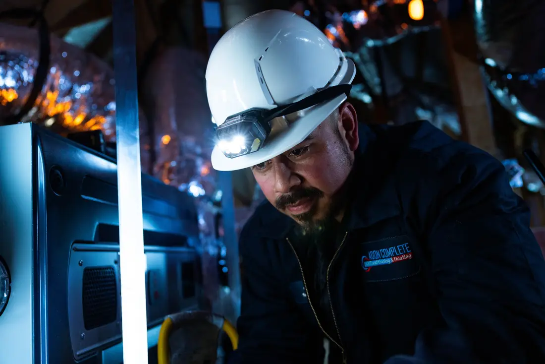 ADON HVAC technician at work in an attic, his hard hat lit by a headlamp