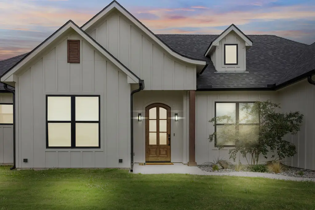 Board-and-batten farmhouse at dusk with the entry light on